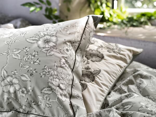 Gambar dekat sarung kuilt dan sarung bantal PRAKTBRÄCKA berwarna kelabu menampilkan corak berbunga-bunga tradisional berwarna hitam putih.