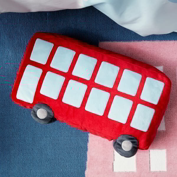 Gambaran dekat kusyen UPPTÅG dalam bentuk bas merah dan dibuat menggunakan poliester kitar semula yang lembut apabila disentuh pipi.