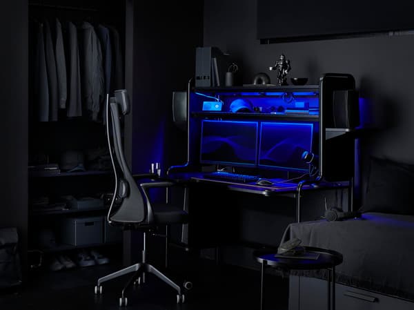 Game set up in een donkere kamer met een zwart bureaustoel aangeschoven aan een zwart bureau.