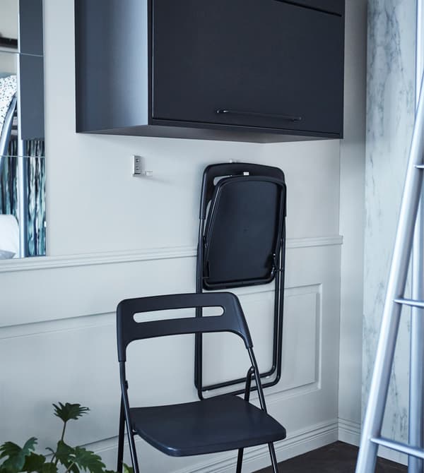 Ganxos d’alumini IKEA BJÄRNUM en una paret utilitzats per penjar cadires plegables.