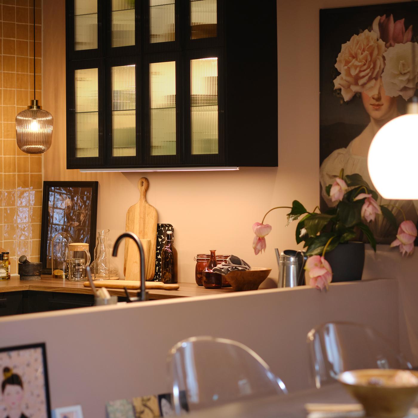 ガラス扉と内側に照明を取り付けたウォールキャビネットや、ワークトップと伸長式テーブルの上につるしたペンダントランプがあるキッチン。