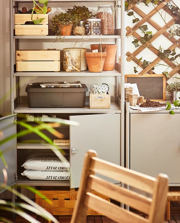 Gardening tools, supplies and potted plants sit in a shelving unit on a balcony.