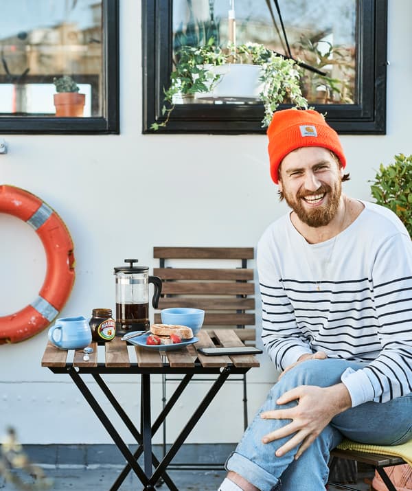 Gareth sentado à mesa com o pequeno-almoço no exterior, na sua casa-barco.