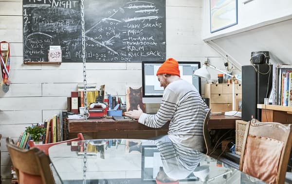 Gareth sitting at his desk with books, a computer and a desk lamp, with a blackboard on the wall above.