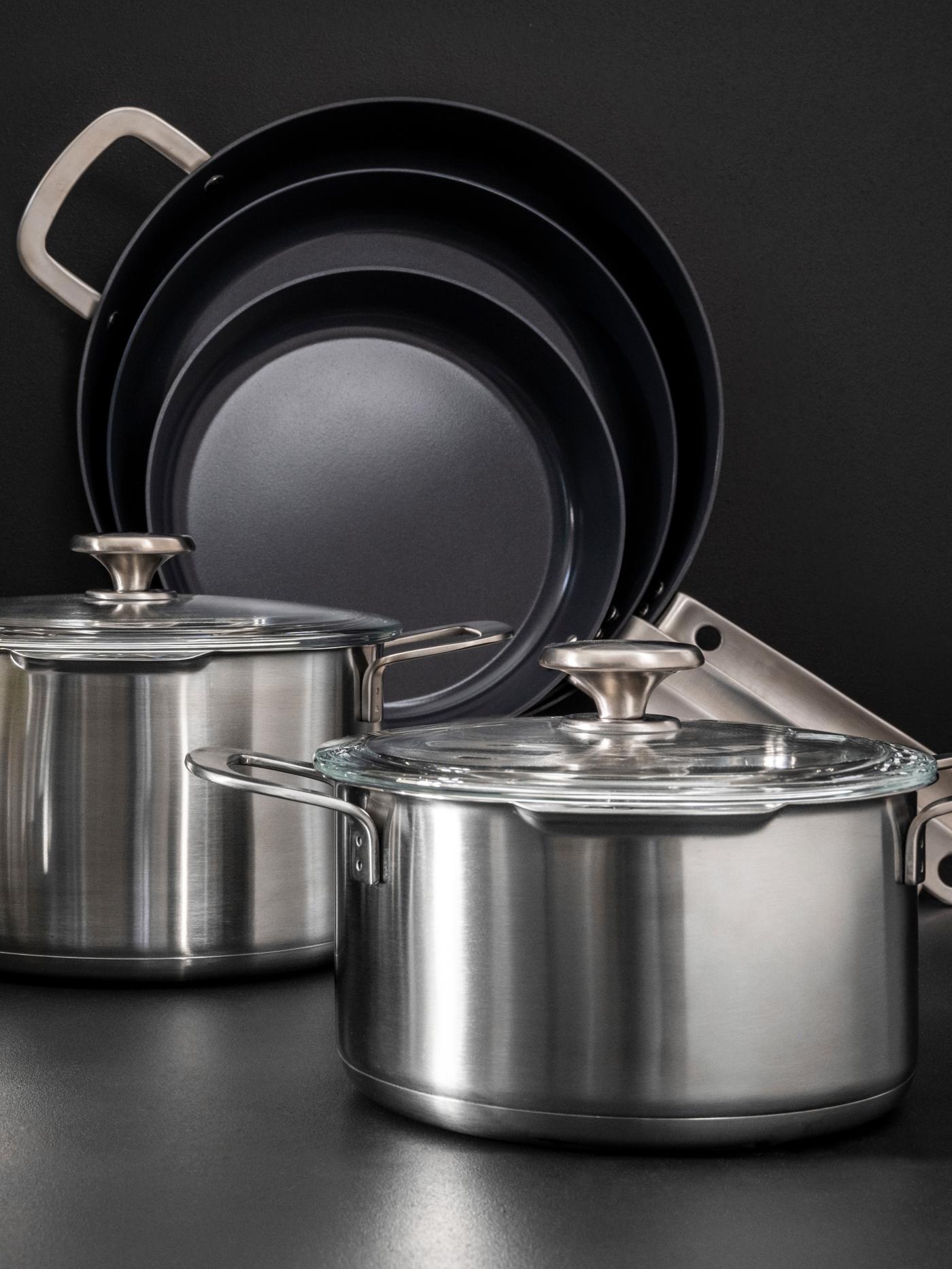 Garnki i patelnie z serii HEMKOMST stoją na czarnym blacie a z tyłu widać czarne tło.