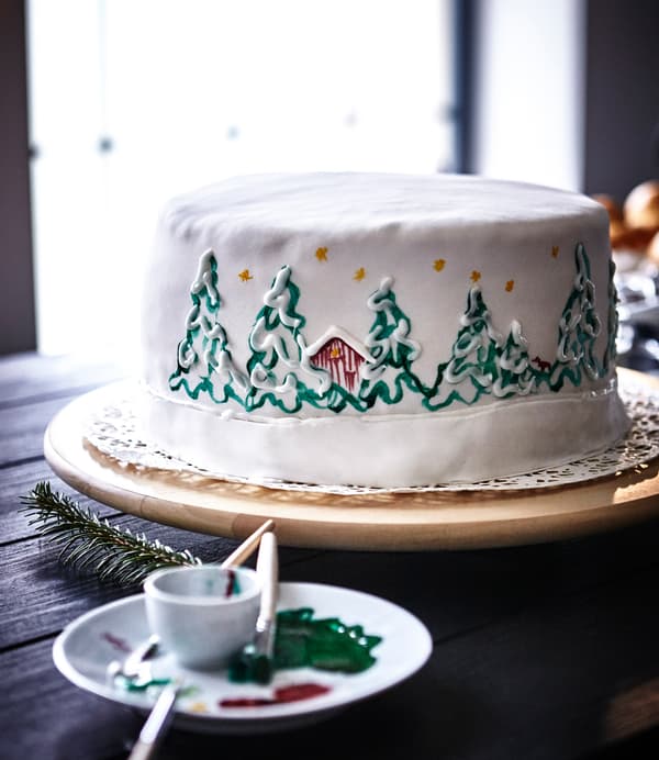 Gâteau blanc avec paysage de Noël peint à la main, présenté sur un plateau tournant IKEA SNUDDA.