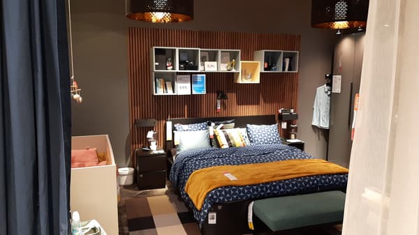 Gemütliches IKEA Schlafzimmer mit modernem Polsterbett, senfgelber Decke und blauen Kissen, dekoriert mit stilvollen Wandregalen und warmem Licht – perfekte Inspiration für die Schlafzimmergestaltung bei IKEA.


