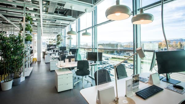 Geoderner IKEA-Showroom mit vielen Arbeitsplätzen am Fenster. Die Räume sind hell und offen gestaltet mit Schreibtischen, Bürostühlen, Lampen und viel Tageslicht durch große Fensterfronten.

