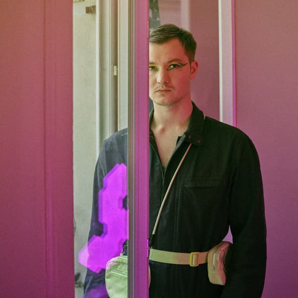 Georgii de face, dans sa chambre derrière une fenetre avec un vetement noir, du maquillage style japonais sur les yeux et des neons roses en arrière plan 