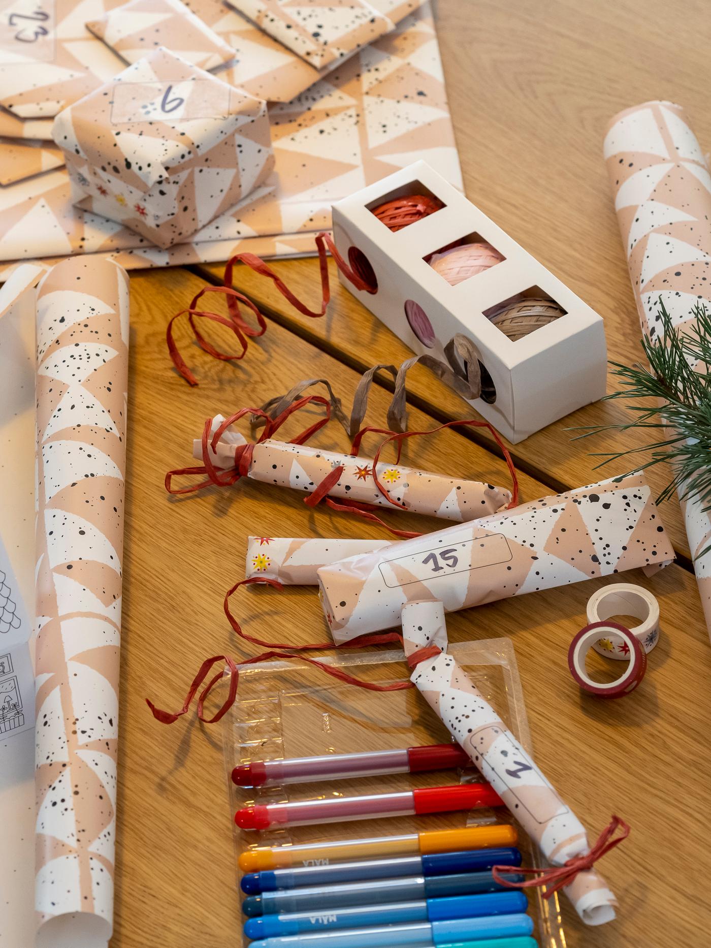 Geschenkpapier, Stifte und Geschenkbänder auf dem Tisch.