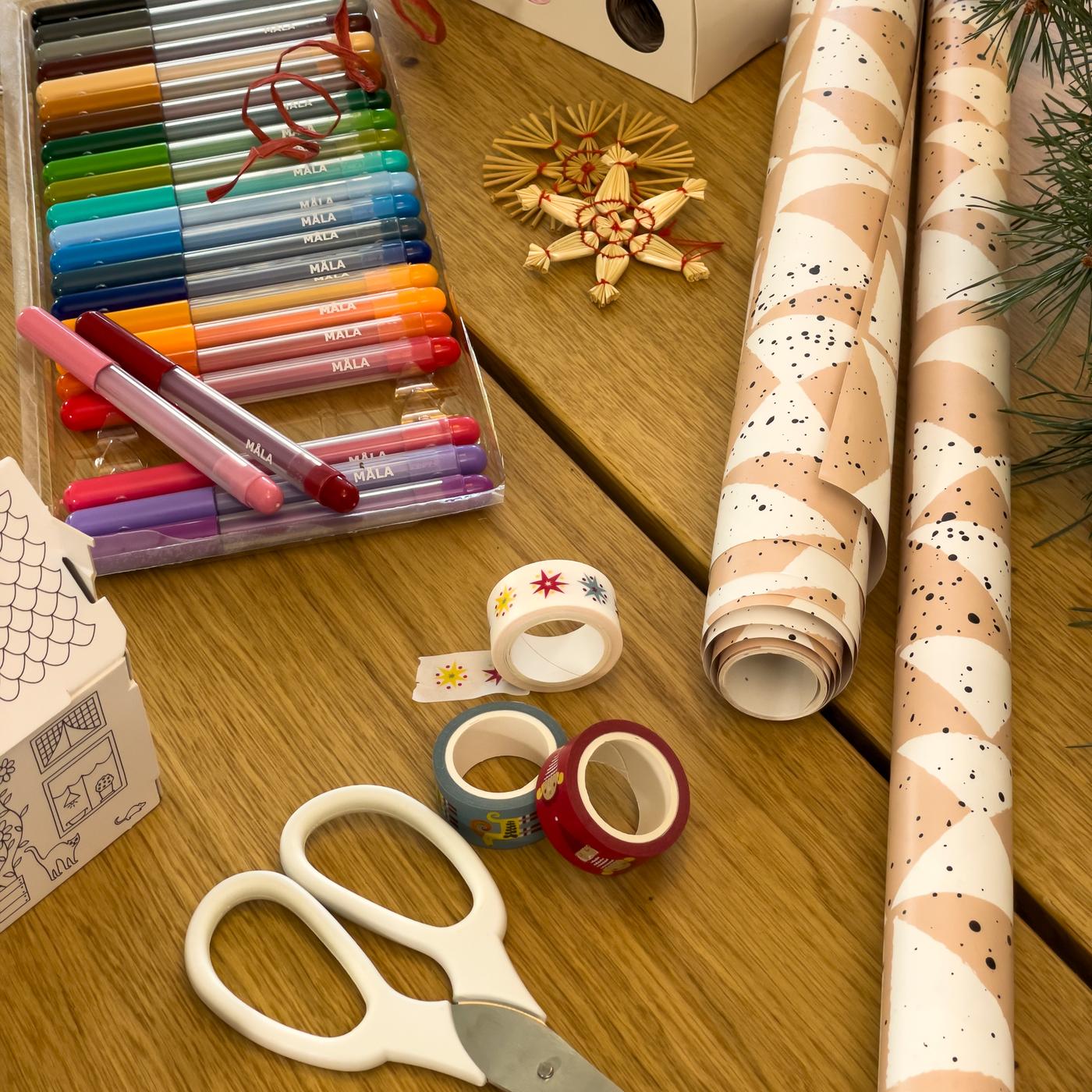 Geschenkpapier, Stifte und Papierband liegen auf einem Tisch.