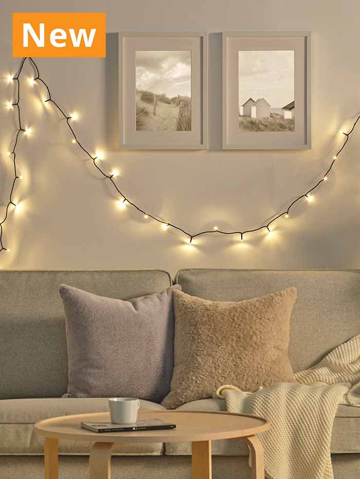 GETKÅL LED string lighting chain, 100cm indoor, hanging across living room wall below photo frames and sofa with cushions.