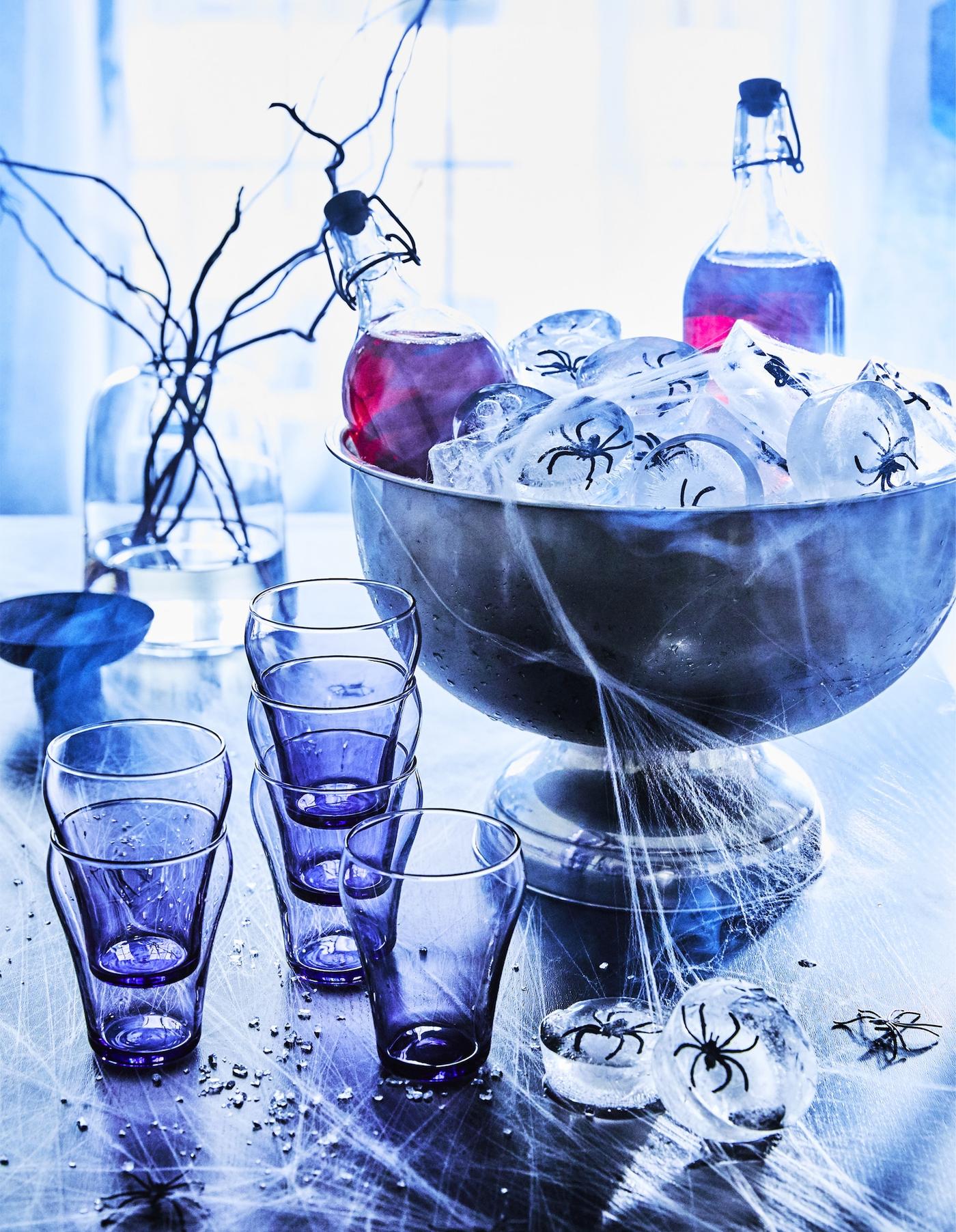 Getränke zwischen Spinneneiswürfeln neben blauen Gläsern