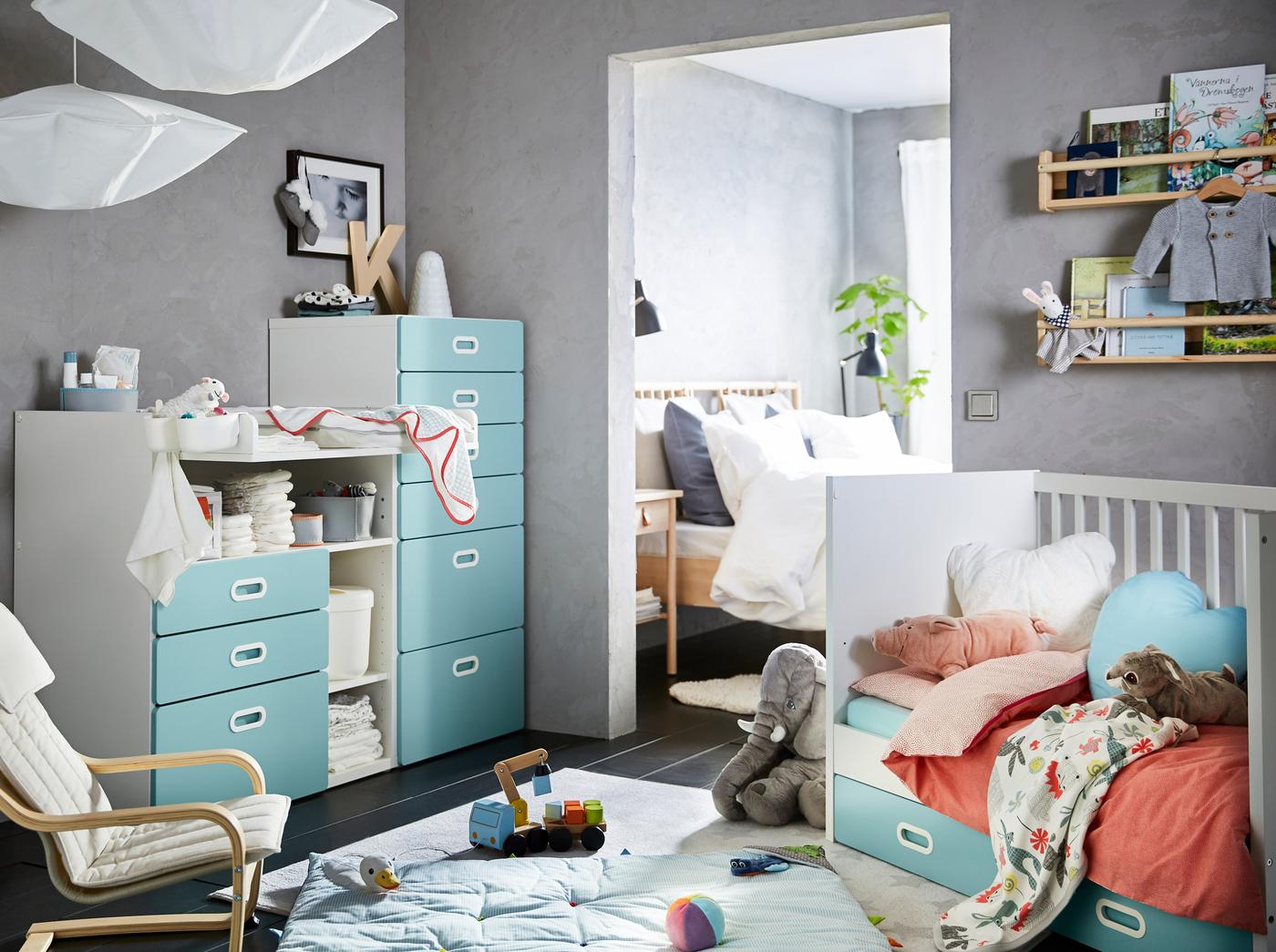غرفة أطفال رضع أزرق، ورمادي، وأحمر وأبيض بيها طاولة تغيير STUVA أبيض وأزرق فاتح، وخزانة ذات 6 أدراج وسرير أطفال.