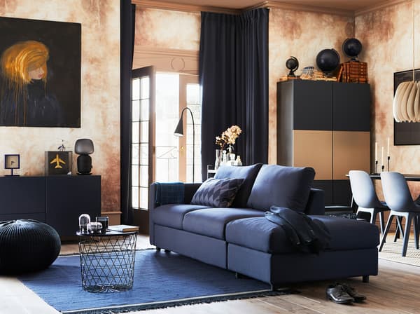 غرفة معيشة مع VIMLE كنبة سرير من 3 مقاعد وغطاء ORRSTA بلون أسود وأزرق وخزائن مختلفة وبعض المقاعد وأبواب فناء مفتوحة.