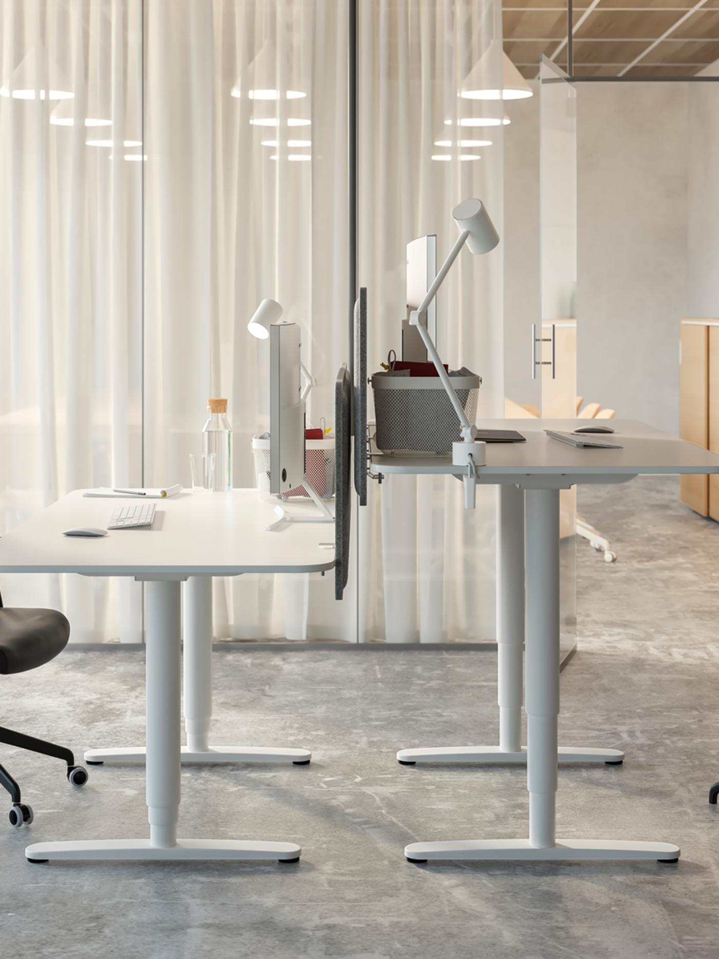 غرفة مكتب تحتوي على مكتبين للجلوس/الوقوف ‪BEKANT‬ قبالة بعضهما البعض، وستائر بيضاء تستخدم كمقسم للغرفة.