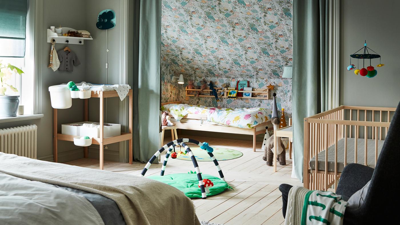 غرفة نوم عائلية تشمل سرير مزدوج وسرير SNIGLAR وسرير أطفال وطاولة تغيير مع ستائر لخلق مساحة خاصة.