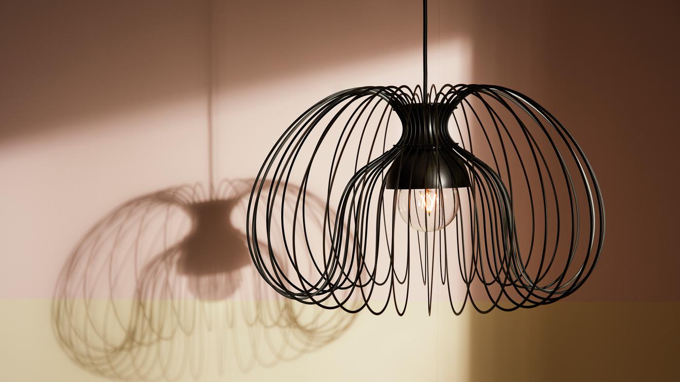 غطاء مصباح معلق معدني KALLFRONT متدلي من السقف يضفي ظلًا مميزًا في الخلفية.