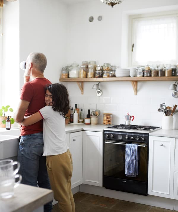 Gigi และลูกสาวกอดกันในห้องครัวสีขาว กระเบื้องผนังสีขาวที่มีโถวางเรียงกันบนชั้นวางยาวทำด้วยไม้