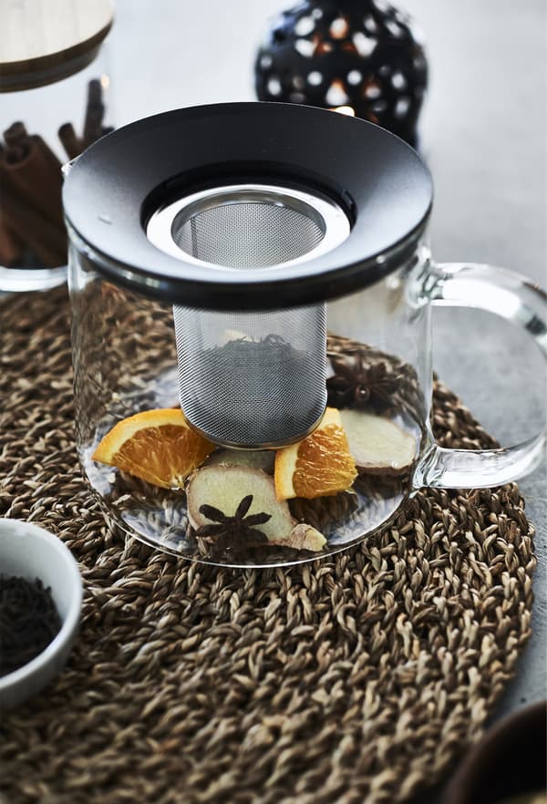 Ginger and orange slices in a glass teapot, sitting on a wicker table mat.