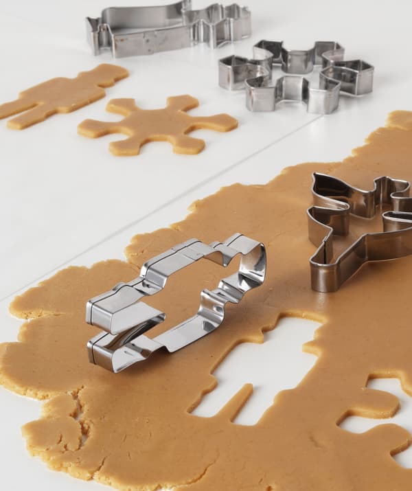 Gingerbread dough carefully rolled out on a table; several pastry cutters involved in cutting out the shape of the biscuits.