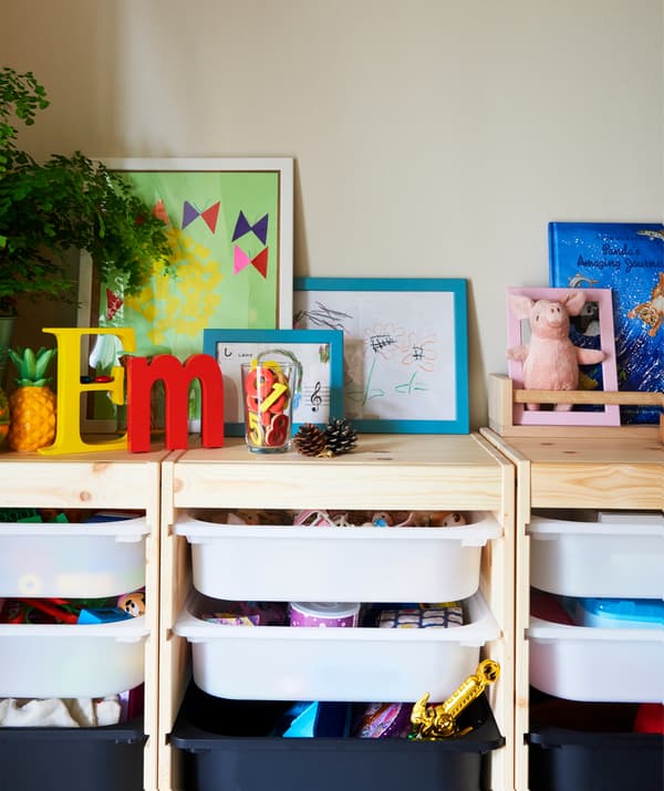 Giocattoli in contenitori estraibili in una struttura in legno con piante, immagini incorniciate e libri.