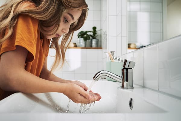 Girl cupping flowing water from a PILKÅN bathroom faucet.