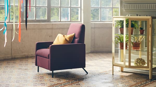 GISTAD recliner in a dark red colour with a yellow cushion placed in its seat, standing in a room with big windows.