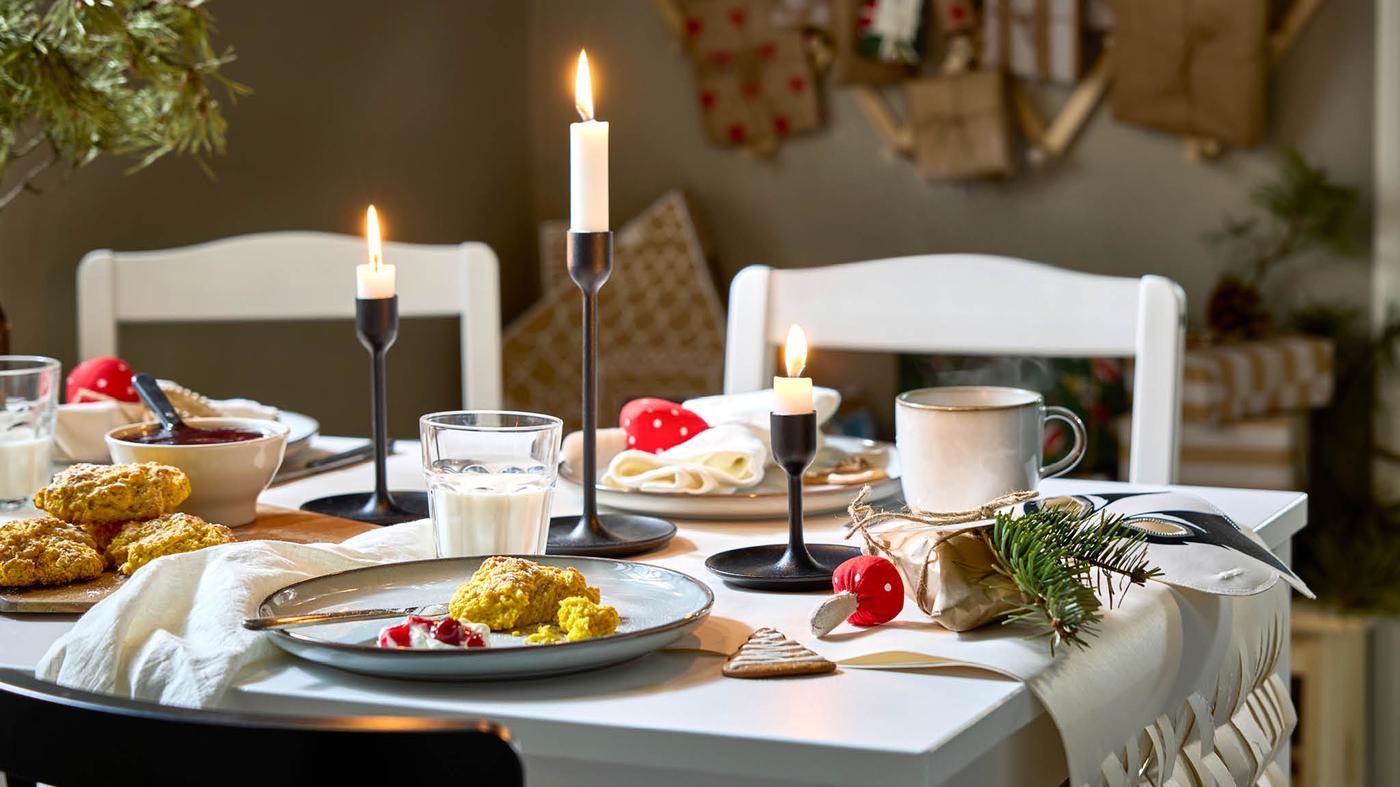 GLADELIG étkészlettel megterített asztal, középen fekete FULLTALIG gyertyatartók, amelyekben JUBLA gyertyák égnek.