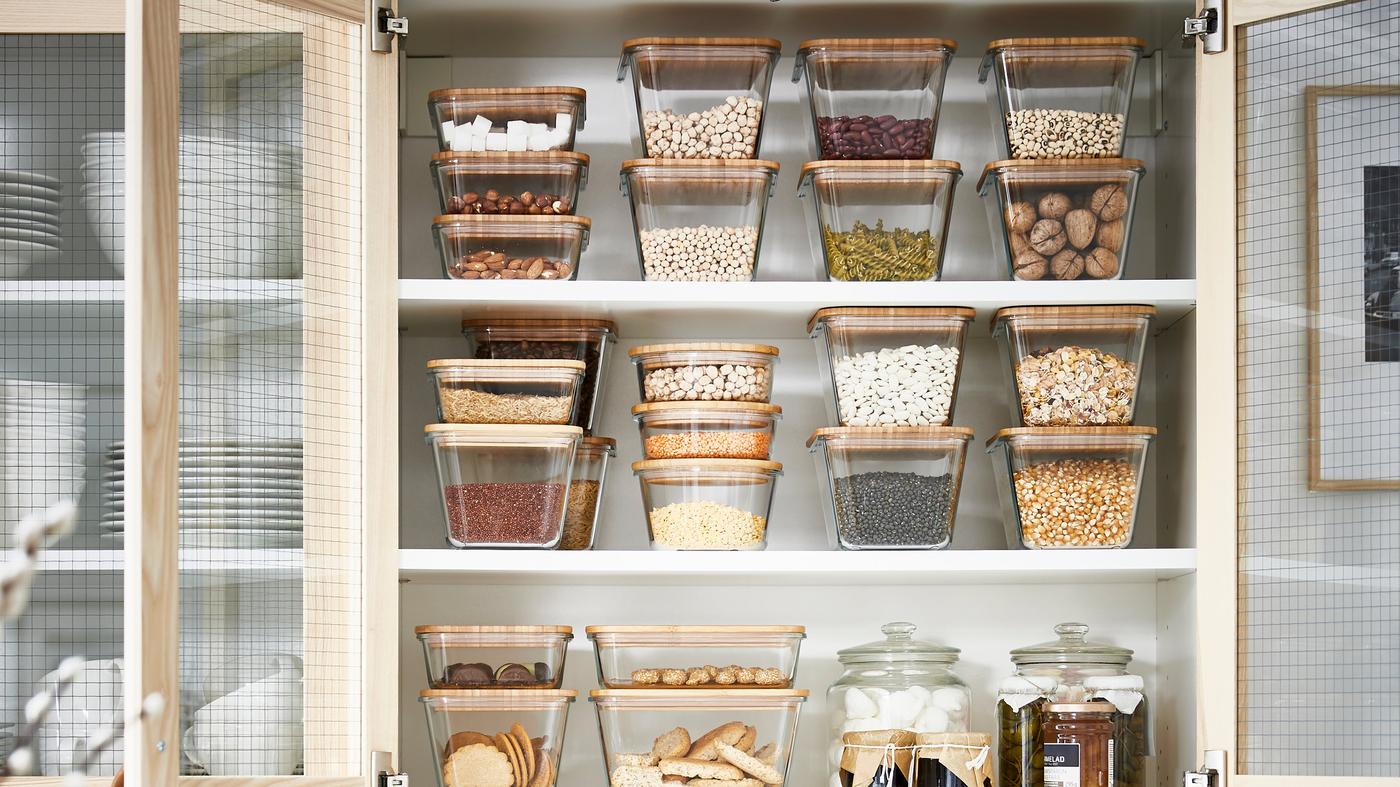 Glasbeholdere med bambuslåg er organiseret og stablet i et køkkenskab.