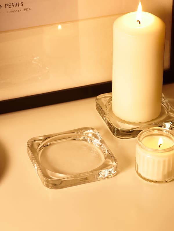 GLASIG top candle holder andADLAD scented candle placed on top of a white table.