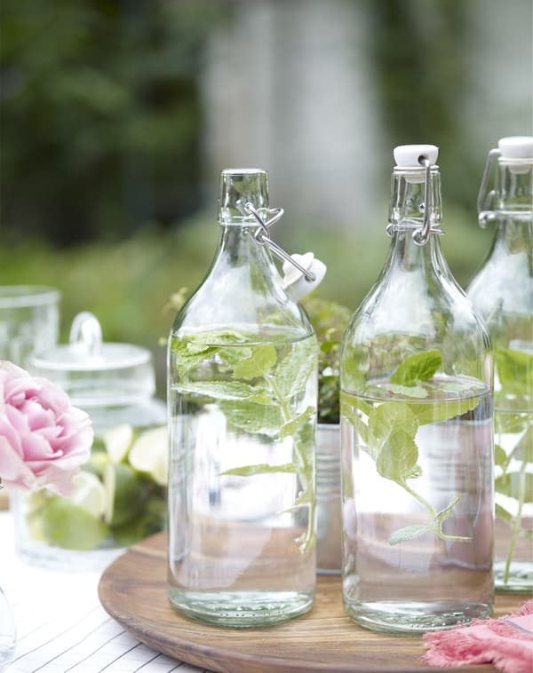 Glass bottles filled with water and aromatic herbs on an outdoor table on a sunny day.