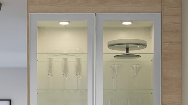 Glass‑door cabinet displaying glassware and cake stands under bright interior lighting.