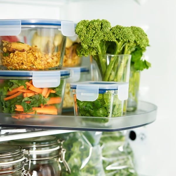 Glass food containers filled with vegetables and leftovers neatly arranged on a fridge shelf.