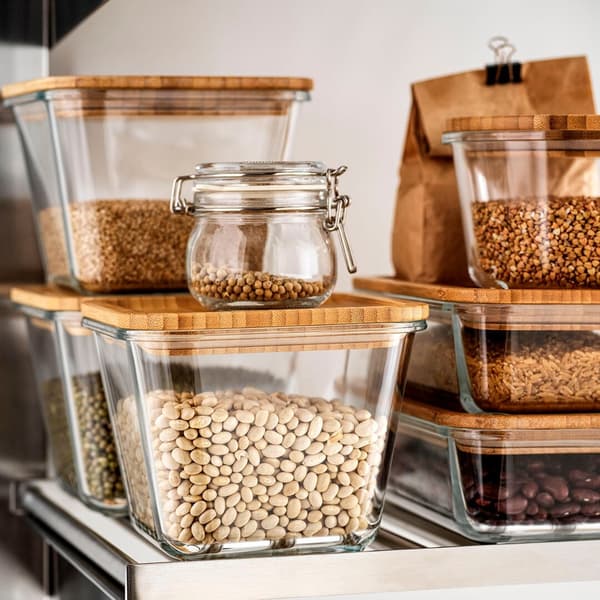 Glass food containers with bamboo lids stacked on top of eachother, all filled with different kind of food.