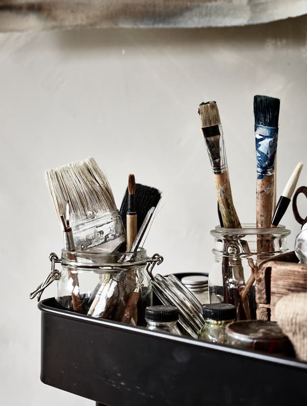 Glass jars  storing paint brushes sit in a metal trolley.