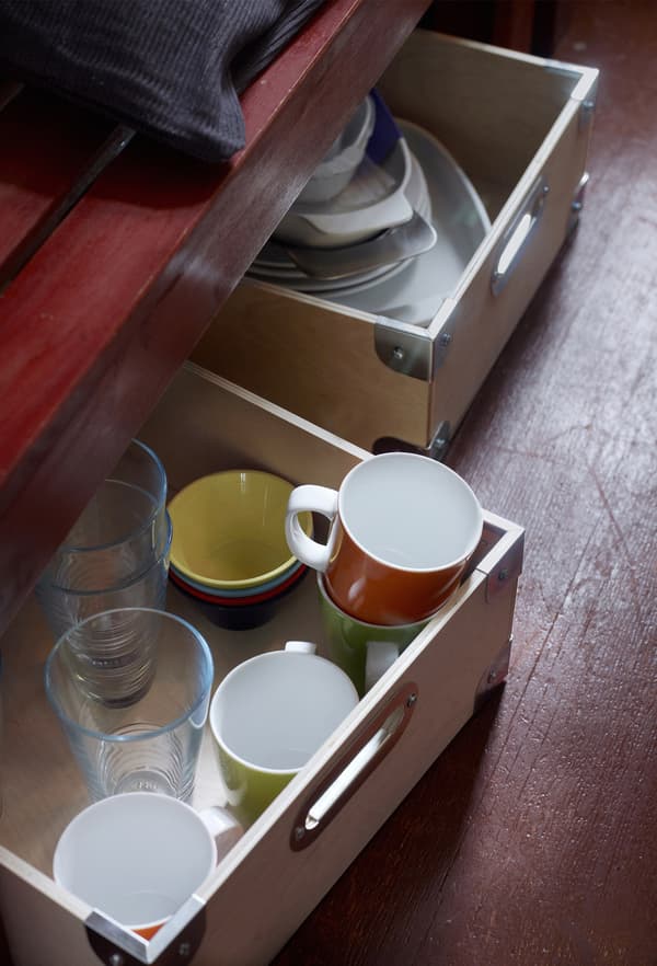 Glasses, mugs, and other kitchen items are stored in wooden boxes under a bench to maximise kitchen storage.