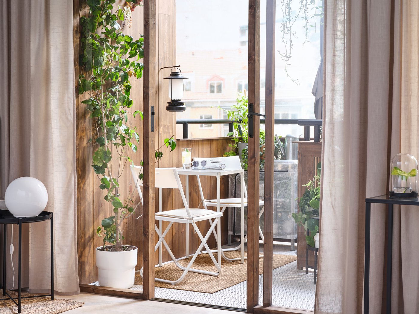 Glasskydedøre fra gulv til loft, indrammet af SILVERLÖNN gardiner, åbner ud til en altan med to FEJAN klapstole.