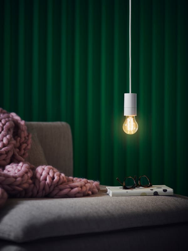 Glödlampa hänger ned i en vit sladd från taket, med grön bakgrund