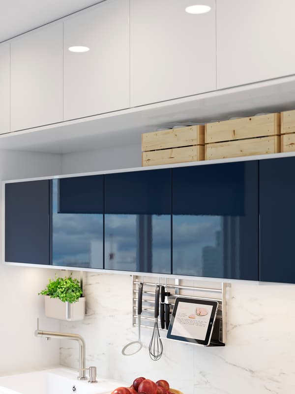 Glossy black-blue wall cabinets above a kitchen counter. A wall grid in stainless steel holds a tablet stand and utensils.
