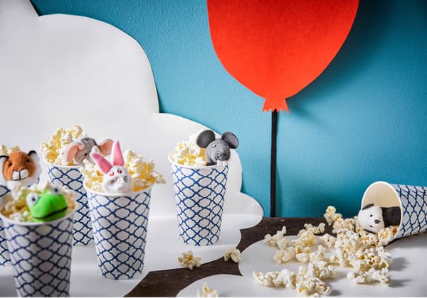 Gobelets en papier remplis de popcorn et décorés d’une marionnette pour doigt. L’un des gobelets déborde de popcorn.