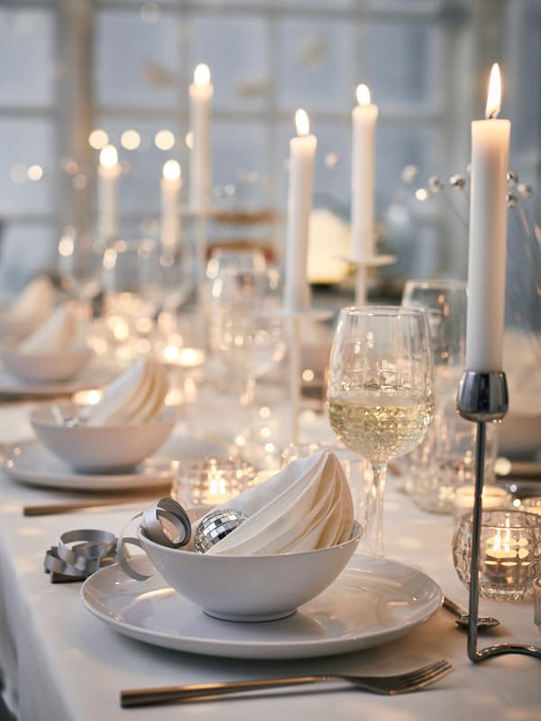 GODMIDDAG tányérok és tálak, FRÖDJA poharak és SILVERPÄRON gyertyatartók égő JUBLA gyertyákkal.