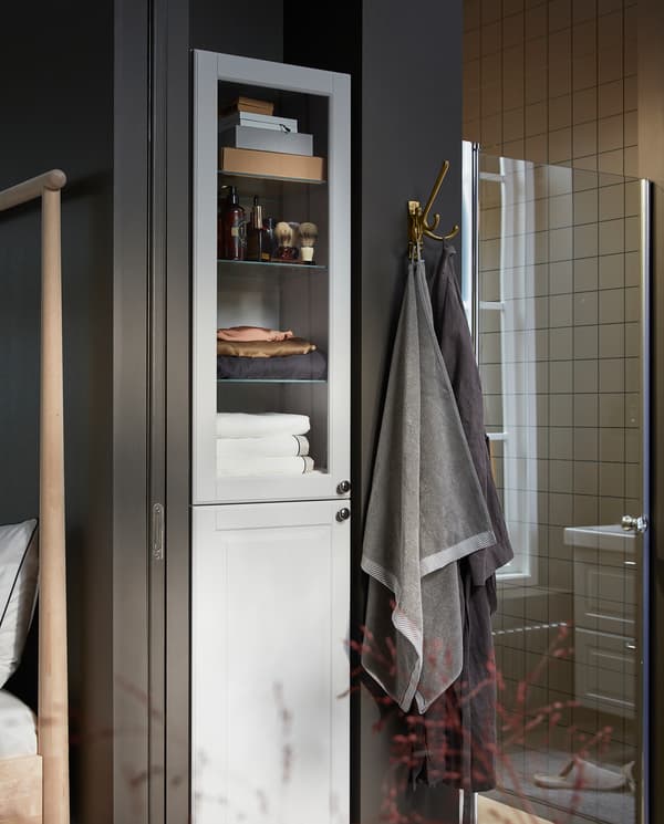 GODMORGON high cabinet in white with a white door and a glass door. Towels and shaving products are stored inside.