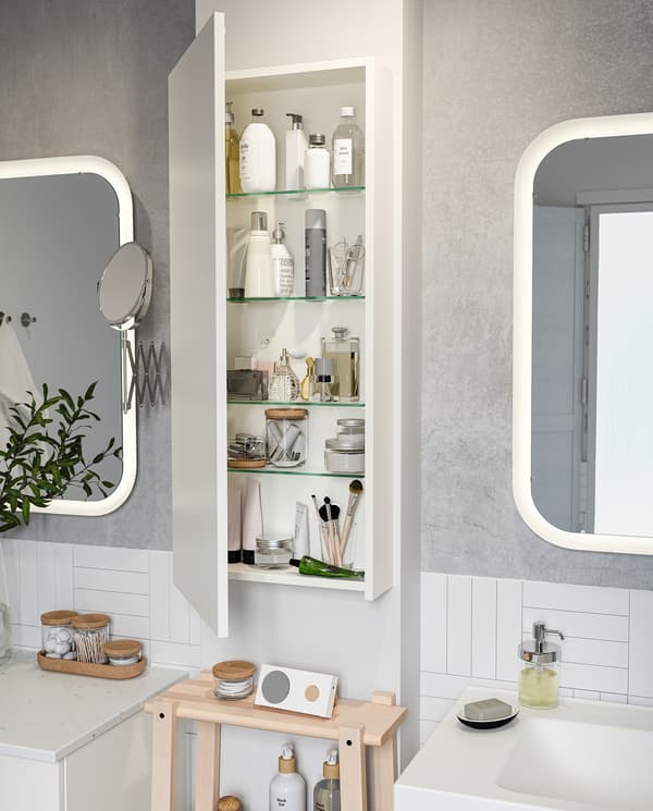 GODMORGON high cabinet is wall-mounted between two bathroom mirrors. The door is open, and products are on the shelves.