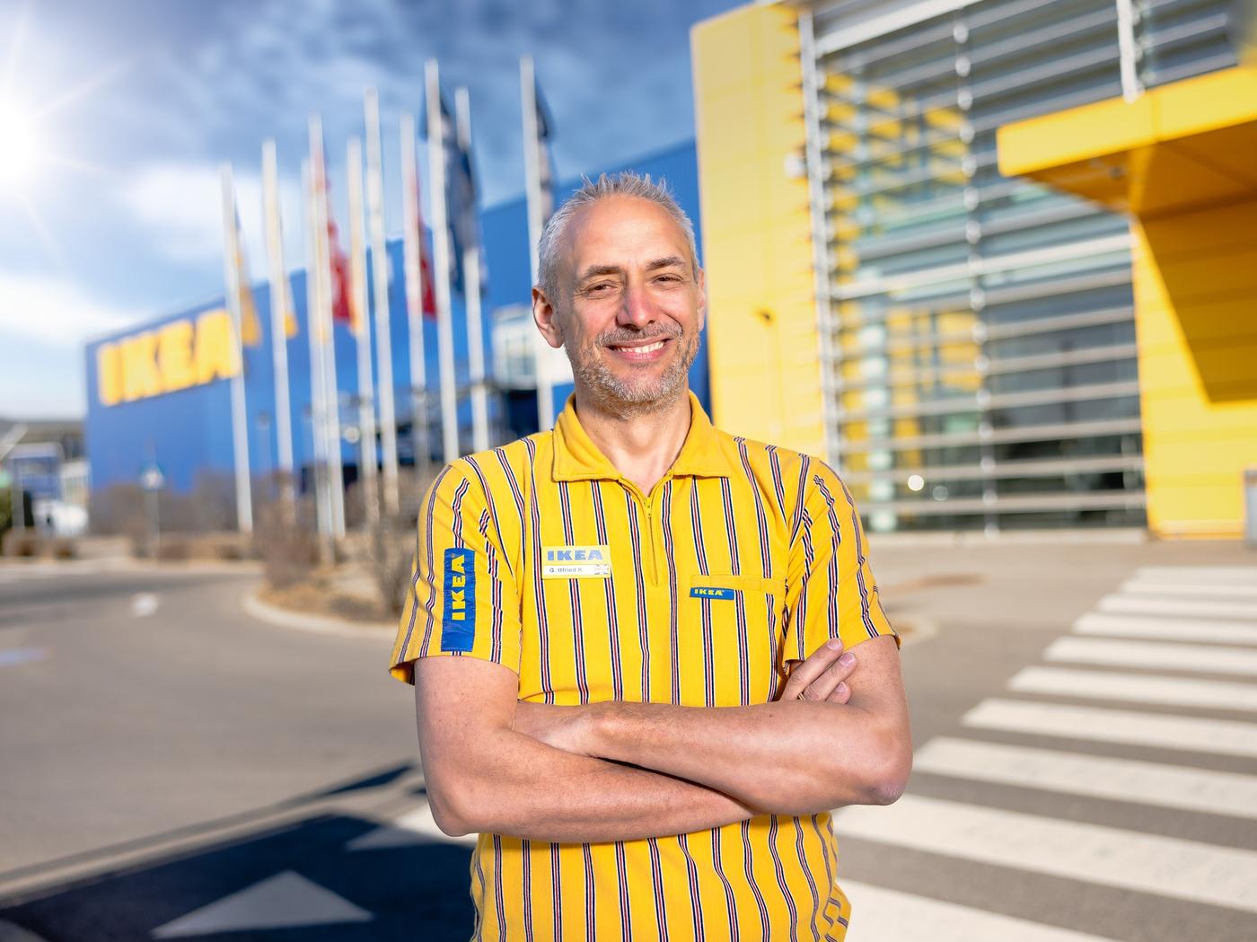 Gottfried Kienzl steht mit verschränkten Armen in einem blau gelb gestreiftem Ikea T-Shirt vor einem Einrichtungshaus