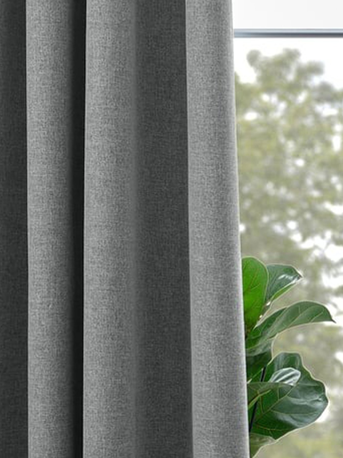 Grå mörkläggande gardiner hänger vid ett fönster med gröna växter i förgrunden.
