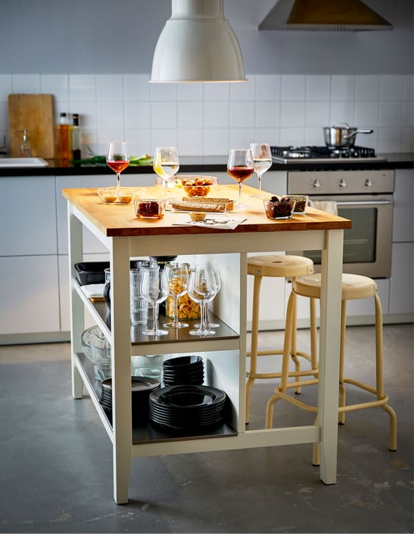 Grand îlot de cuisine avec snacks et verres à vin, avec vaisselle rangée sur les tablettes du bas.