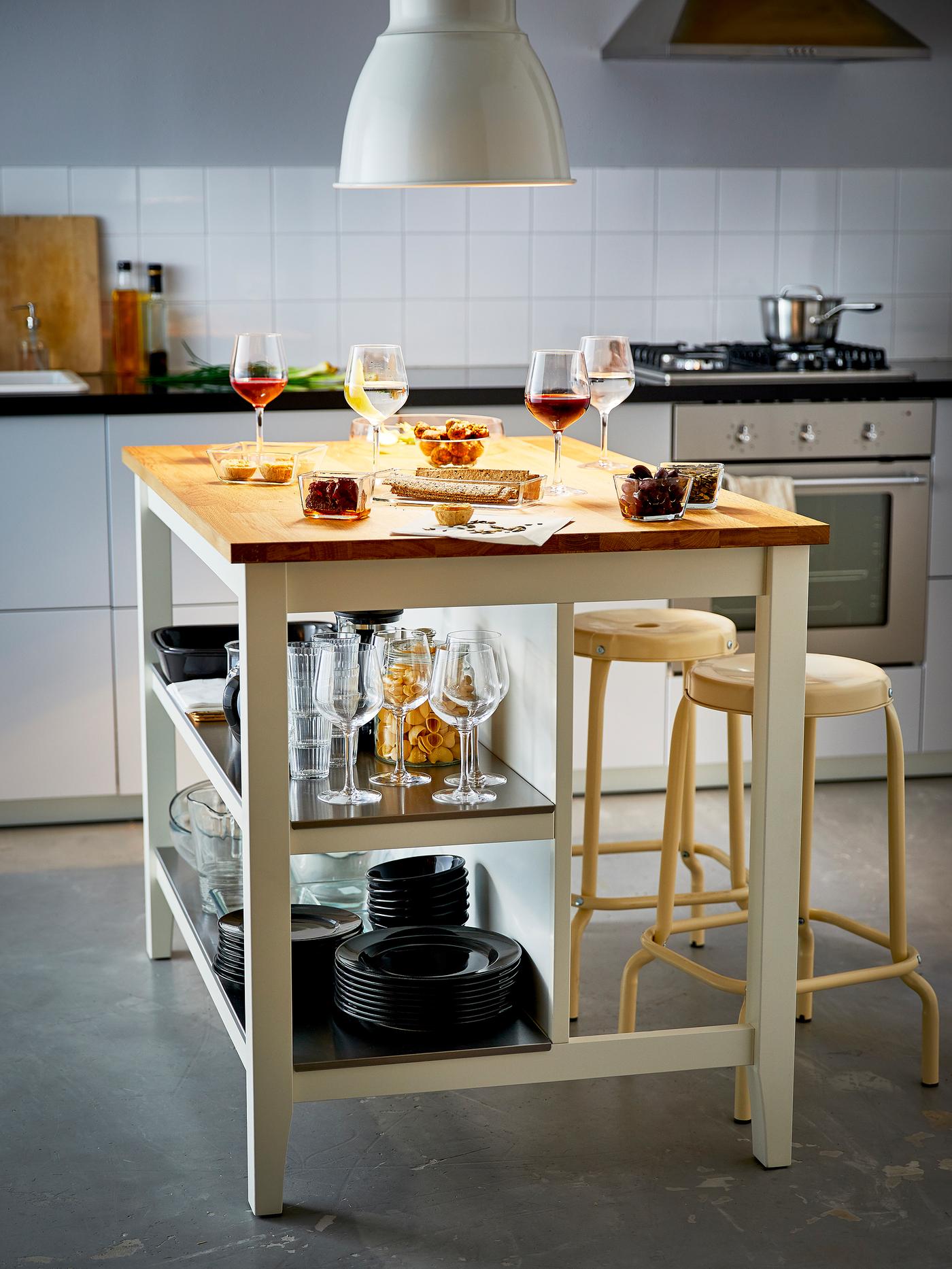 Grand îlot de cuisine avec snacks et verres à vin, vaisselle rangée sur les tablettes du bas.
