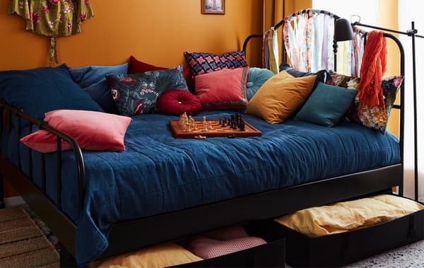 Grand lit garni de nombreux coussins, jeu d’échec posé sur la couette. Draps et couvertures rangés dans des coffres sous le lit.