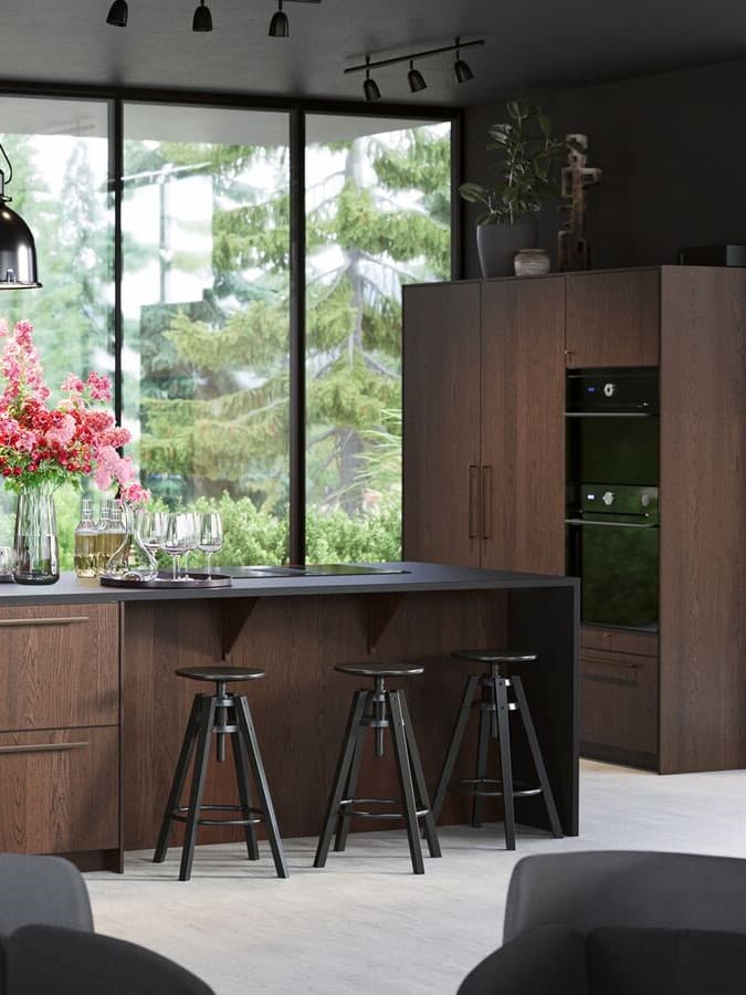 Grande isola per cucina con frontali in legno. Sgabelli bar neri, lampade a sospensione nere e frigorifero con ante in legno.